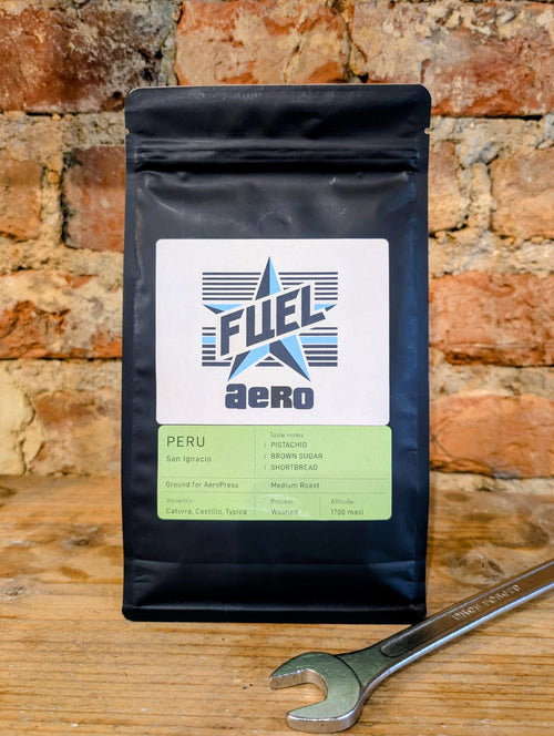 Bag of Fuel Aero Peru single origin coffee, ground for AeroPress, on a shelf in front of a brick wall with a retro spanner