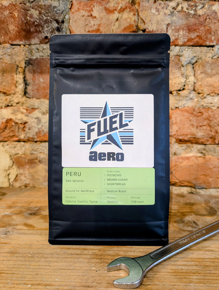 Bag of Fuel Aero Peru single origin coffee, ground for AeroPress, on a shelf in front of a brick wall with a retro spanner