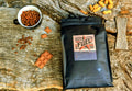 Fuel Premium whole bean coffee bag beside coffee beans and milk chocolate on a weathered wooden log